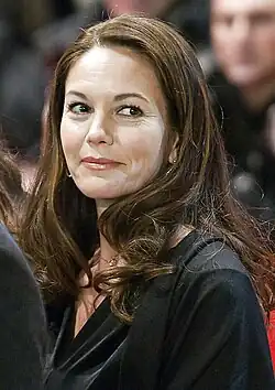 Diane Lane auf dem roten Teppich der Berlinade 2012 lächelt leicht und schaut zur Seite. Sie hat lange, wellige, braune Haare und trägt ein dunkles Kleidungsstück. Sie hat eine Kette mit einem kleinen Anhänger um den Hals. Im Hintergrund des Bildes kann man wartende Personen, die unscharf im Hintergrund zu erkennen sind. Der Fokus liegt auf den Haaren, der Kleidung und den Accessoires von Diane Lane, die am wartenende Fotografen vorbei geht.