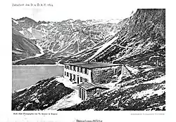 historische Schwarz-Weiss-Aufnahme aus dem Jahr 1894, Schrägaufnahme eines zweigeschossigen Gebäudes, der Douglasshütte; Seitenwand wirkt grober als Fassade; im Hintergrund der Lünersee