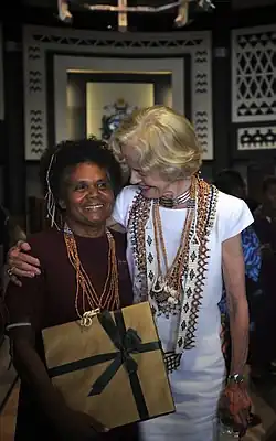 Alice Pollard mit der australischen Generalgouverneurin Quentin Bryce. Eine kleinere polynesische Frau mit Kraushaaren und einem großen flachen Geschenk und eine australische Frau im weißen Kostüm mit zahlreichen traditionellen Perlenketten.