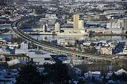 Foto einer Stadt, die an einem Fluss liegt, über die eine Straßenbrücke führt.