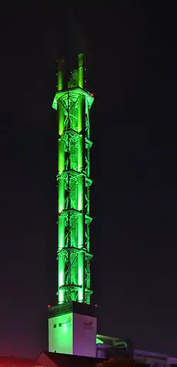 Stadtwerketurm mit den Unterbauten des HKW II sowie den Ersatzschornstein für HKW I und Heizwerk im Hintergrund (links, 2014); Nachtaufnahme mit der charakteristisch grünen Beleuchtung (2012)