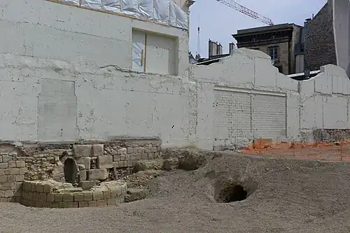 Sockel eines Turms der Stadtmauer Philipps II., der 2015 bei den archäologischen Grabungen im Institut de France vor dem Bau eines neuen Gebäudes entdeckt wurde. Der Verlauf der Stadtmauer bildet auch die Grenze zwischen dem Institut de France und der Monnaie de Paris. Man erkennt auch den Eingang eines von Louis Le Vau konstruierten Abwasserkanals im ehemaligen Mauergraben anlässlich des Baus des Collège des Quatre-Nations im 17. Jahrhundert[46].