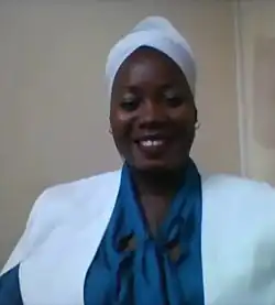 Elsa Garrido, eine dunkelhäutige Frau mit dunkelblauer Bluse, einer weißen Jacke und einem weißen Kopftuch nach afrikanischer Mode.