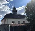 Ansicht von Norden, Kirche hinter Wehrmauer und Bushaltestelle
