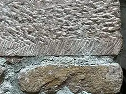 Der obere Stein weist deutliche Bearbeitungsspuren, d.&nbsp;h. eine Faktur, auf. Der untere Stein ist unbearbeitet und zeigt eine körnige, unregelmäßige Textur.