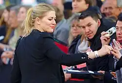 Nina Bott auf dem rotem Teppich der Deutschlandpremiere von "Zulu" schreibt Autogramme für hinter einer Absperrung stehenden Fans, die auf die Stars warten und Fotos machen. Nina Bott im schwarzen Blaser reicht einem Fan seinen Stift herüber. Am Handgelenk ein weißes Plastikarmband, welches Einlass zur Premiere gibt mit der Aufschrift des Veranstalters des Cinemaxx in Hamburg am 6. Mai 2014.