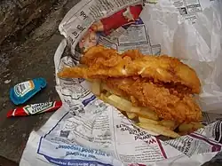 Fish ’n’ Chips mit Papierschutz vor der Druckerschwärze der Zeitung und Soßenbeutel