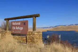 Eingangsschild zum National Elk Refuge mit dem Feuchtgebiet des Flat Creek im Hintergrund