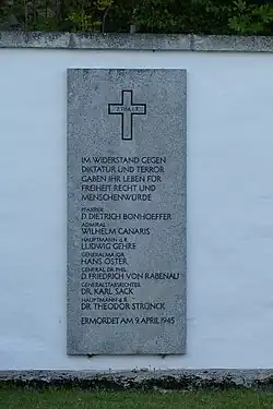 Grauer Gedenkstein an einer weißen Mauer mit den eingemeißelten Namen der am 9. April 1945 in Flossenbürg ermordeten Mitglieder des Widerstandes: Dietrich Bonhoeffer, Wilhelm Canaris, Ludwig Gehre, Hans Oster, Karl Sack, Theodor Strünck