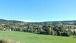 Aufnahme einer hügeligen Landschaft, die teils bebaut und teils bewaldet ist und teils Wiesen hat
