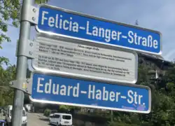 zwei Straßenschilder mit dem neuen und alten Namen der zu Ehren von Felicia Langer umbenannten Straße mit Zusatzschild mit biographischen Informationen zu Frau Langer und einer Begründung der Umbenennung.
