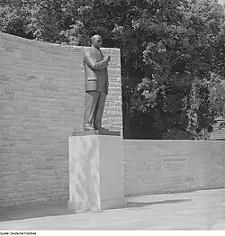 Ein schwarz-weiß-Foto zeigt das Bronzestandbild des Ernst Thälmann in Stralsund im Jahr 1962 vor einer hohen Mauer, an der halbhohen Mauer daneben ist eine Gedenkplatte mit den Lebensdaten Thälmanns angebracht.
