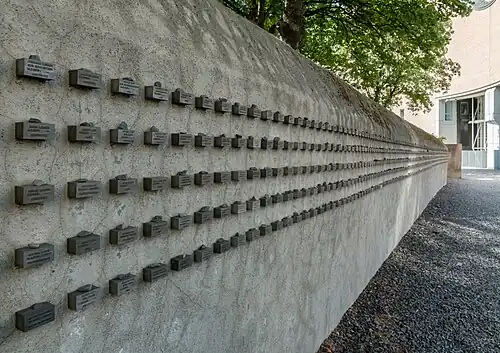 Namensblöcke als Fries an der Außenmauer des Friedhofs