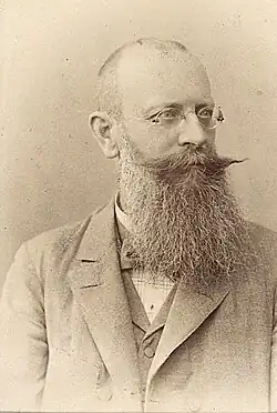 Friedrich Stolz mit kleiner Rundbrille, langem Bart, Fliege und im Anzug