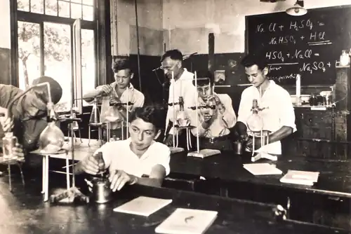 Chemieunterricht in der Schulgemeinde Wickersdorf, ca. 1934/35. Lt. Tafel beschäftigen sich Schüler und Lehrer u.&nbsp;a. mit einer Reaktionsgleichung, bei der es darum geht, dass eine stärkere Säure die schwächere aus ihrem Salz verdrängt[92]