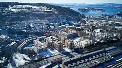 Drohnenaufnahme einer an der Küste gelegenen Stadt. Im Vordergrund Wohnblöcke, etwas entfernt steigt das Terrain an.