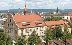 Gebäude des Stadtarchivs Bamberg mit roten Ziegeldächern und mittigem Dachreiter, umgeben von Bäumen und Stadtpanorama im Hintergrund