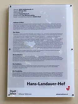 Es handelt sich um die Aufnahme einer Gedenktafel zur Erinnerung an den Spanienkämpfer Hans Landauer (1921–2014) an der Fassade einer städtischen Wohnanlage in Wien.