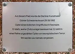 Metallplakette mit der Aufschrift „Auf diesem Platz wurde der Berliner Kunstmaler Günter Schwannecke am 29.08.1992 Opfer eines tödlichen Angriffs durch Neonazis. Er starb, weil er Zivilcourage bewiesen hat. Er steht in einer Reihe ungezählter Opfer von neonazistischem Terror. Wir werden sie niemals vergessen.“