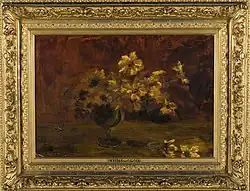 Das Gemälde im verzierten Goldrahmen stellt gelbe Blumen in einer Glasvase mit schlankem Stiel dar. Der Hintergrund ist verschwommen.