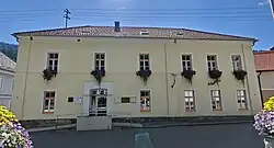 Zweistöckiges Gebäude mit hellgelber Fassade und Blumenkörbe an den Fenstern im Obergeschoß