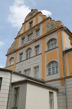 Nordwest-Giebel des Stadtarchivs Bamberg mit gelb-weißer Fassade, mehreren Fenstern und der Aufschrift ‚STADTARCHIV‘ unter blauem Himmel