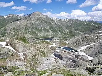 Blick auf die Südwestwand des Monte Prosa im Sommer, am Fuss des Berges der Lago della Piazza, rechts davon die Gebäudegruppe mit u. a. dem Hotel Ospizio San Gottardo