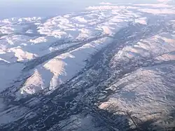Luftbild einer Landschaft, die von schneebedeckten Bergen geprägt ist. Durch diese Landschaft führen einige Täler, im Vordergrund zieht sich ein etwas breiteres Tal mit einem Fluss durch die Landschaft