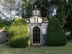 Mausoleum von Karadjordjevic in Genf. Bau im Stil einer orthodoxen Kirche mit Kuppel zwischen zwei Eibenbüschen. Die Front ist mit Kreuzen, Weinranken und einem Wappen verziert.