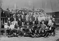 Schwarzweißfoto der Mitglieder, die sich in sieben Reihen formiert haben. Die vorne liegenden halten Bierkrüge in der Hand.