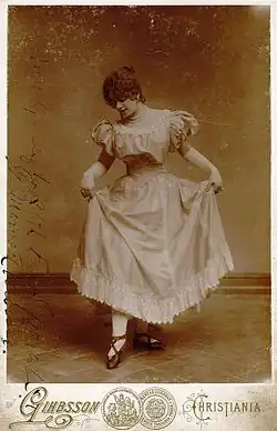 Profilfoto in Sepia: junge Frau mit dunklen lockigen Haaren in Balettpose im knöchellangen Rüschenkleid