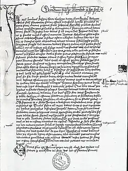 Im Text ist die Seite einer Handschrift in lateinischer Schrift zu sehen. Der Text ist in eine Überschrift und einen Korpus gegliedert. An den Rändern stehen einige Wörter. In der linken oberen Ecke ist eine Verschnörkelung zu sehen.