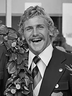 Auf diesem Schwarzweißfoto ist Hans Smits im Anzug mit Krawatte zu sehen, als die Mannschaft bei der Rückkehr von den Olympischen Spielen in Montreal mit Blumen begrüßt wird.