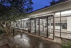 Der Haupteingang des TIB-Standorts Sozialwissenschaften im Theodor-Lessing-Haus, umgeben von Bäumen, mit Weg und Fahrradständer.