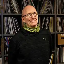 Helmut Philips steht vor einem Plattenregal und schaut reserviert in die Kamera