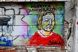 Bild einer Frau mit blonden halblangen Haaren im roten Kleid auf einer Mauer, vermutlich gesprüht