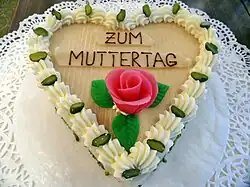 Das Foto zeigt eine herzförmige Torte mit einer Marzipanrose und der Aufschrift „Zum Muttertag“.