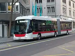 Ein Gelenktrolleybus an einer Haltestelle vor einem Geschäftshaus
