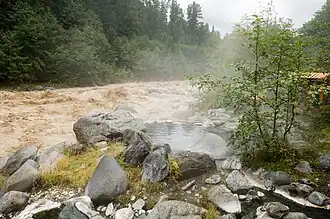 Ein dampfendes Wasserbecken umgeben von einer Gruppe von Felsen in der Nähe eines schlammigen Flusses