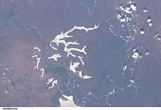 Satellitenbild einer von einem Fluss durchzogenen Seenlandschaft. Die Gebiete entlang des Flusses erscheinen grün, der Rest der Landschaft eher bräunlich.