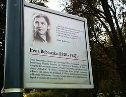 Eine Gedenktafel mit einem Porträt von Irena Bobowska ist an einem Straßenmast angebracht. Der Hintergrund ist weiß und in polnischer Schrift ist ein Zitat und biografische Inhalte eingebunden.