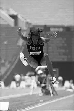 Schwarzweiß-Foto: Eine Frau springt mit nach vorne gestreckten Armen und Beinen. Ein Bein ist angewinkelt.