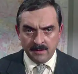 Mann im mittleren Alter von vorn im dunklen Blazer, hellem Hemd und grauer Krawatte ab Schulterblatt in Farbe.