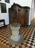 Romanischer Taufstein der ursprünglichen Kirche, im Hintergrund ein spätbarocker Beichtstuhl