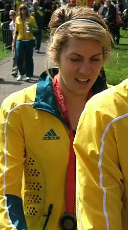 Jenna Santoromito trägt eine gelbe Trainingsjacke mit grünem Kragen. An einem roten Band um ihren Hals ist die Bronzemedaille erkennbar.