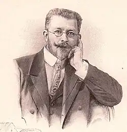 Jules-Alexis Muenier. Zeichnung in Sepia. Ein Mann mit Bart und gezwirbeltem Schnurrbart und kleiner runder Brille in Denkerpose mit der linken Hand an der Backe.