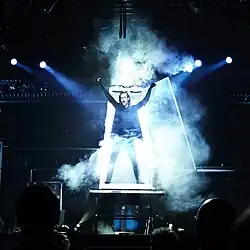 Zauberer Julius Frack steht mit erhobenem Arm umgeben von Bühnennebel zur Eröffnung seiner Magie-Show in einem Plexiglaskabinett als Erscheinungsillusion