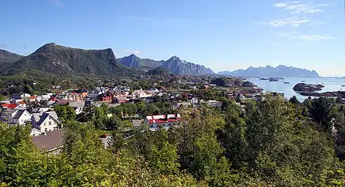 Foto einer an der Küste gelegenen Ortschaft, im Hintergrund Berge und Inseln