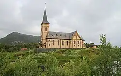 Foto einer Holzkirche, im Hintergrund eine Erhebung