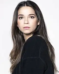 Karolina Sawka (2020) zeigt eine Person mit langen, dunklen Haaren, die ein schwarzes Oberteil trägt. Sie schaut direkt in die Kamera mit neutralem Gesichtsausdruck. Der Hintergrund ist schlicht und weiß